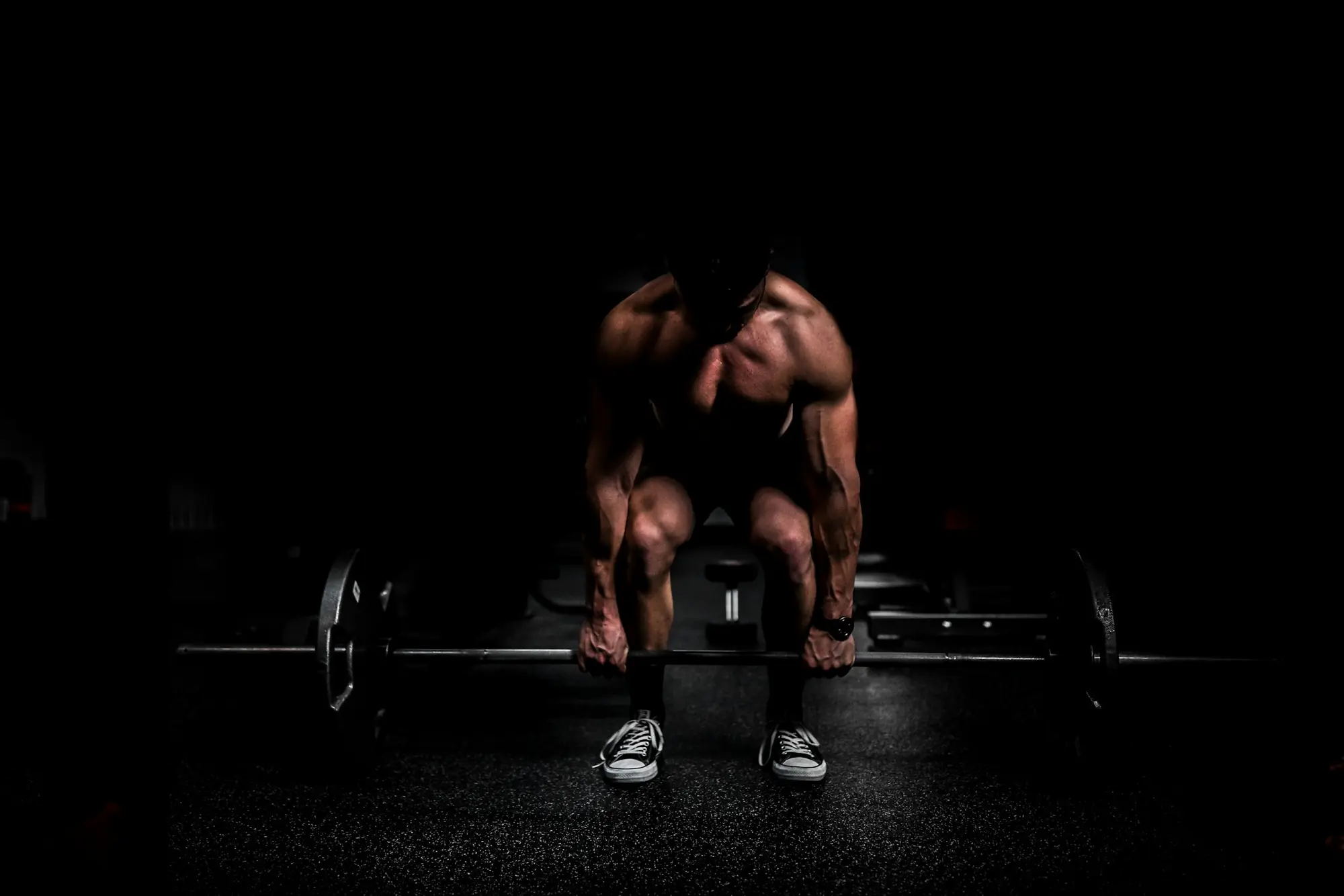 A lifter setting up a barbell deadlift in low light
